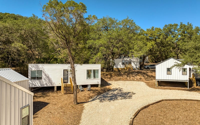 Modern tiny home rentals with white exteriors and wooden stairs, set along a winding gravel pathway in a wooded countryside setting.