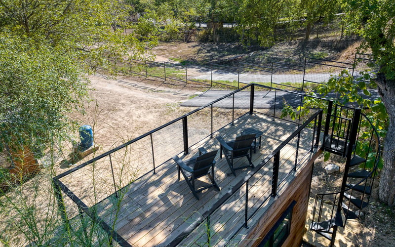 Private rooftop deck with two lounge chairs, black metal railing, and a spiral staircase, overlooking a scenic wooded landscape at a vacation rental.