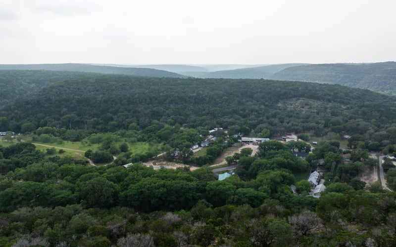 Aerial view of Texas Hill Country surrounded by dense green forest and rolling hills under a cloudy sky.