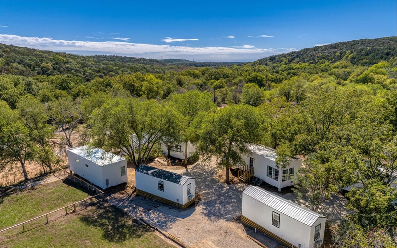 Modern tiny home New Braunfels Vacation Rental nestled among trees, with gravel pathways and scenic hillside views in the countryside.